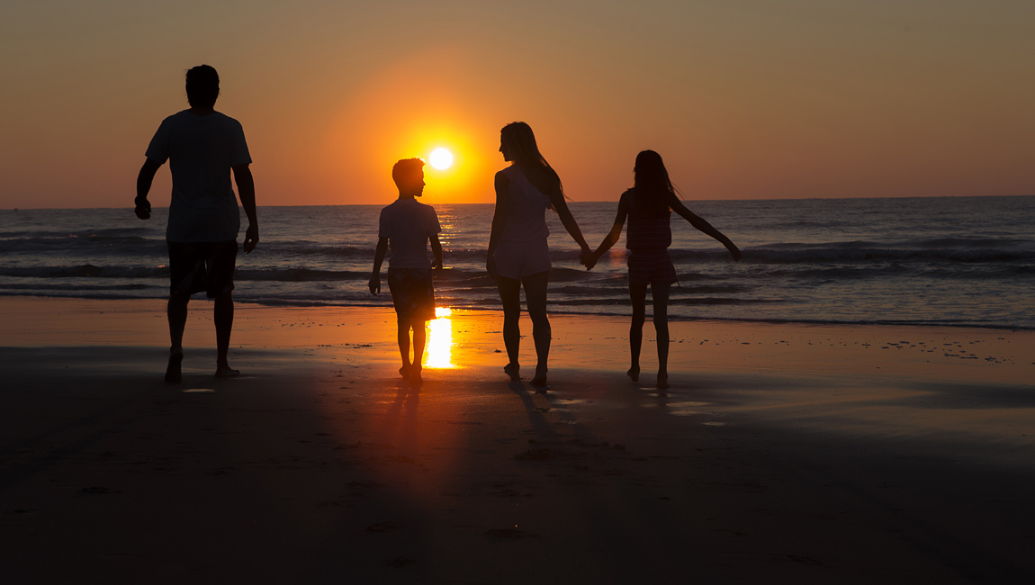 A family of four walks along the beach at sunset.