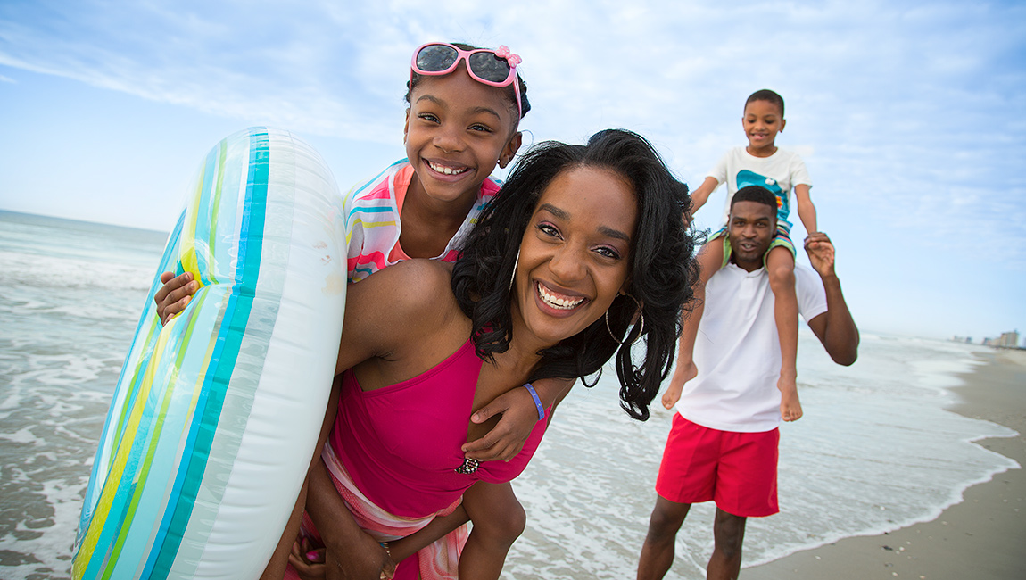 A family of four is posing on the beach, smiling and having fun.