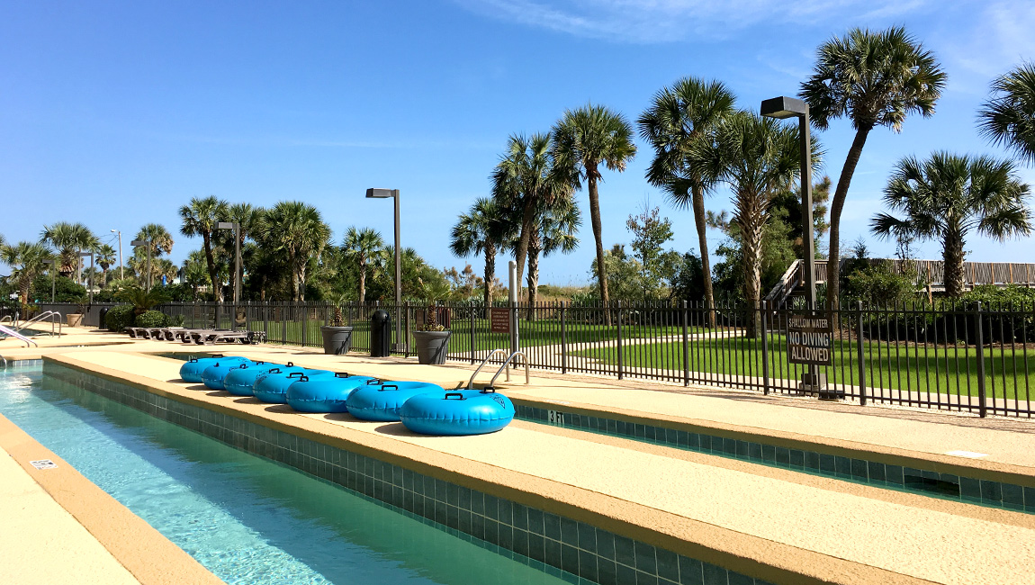A fenced pool area with blue inner tubes and palm trees in the background.